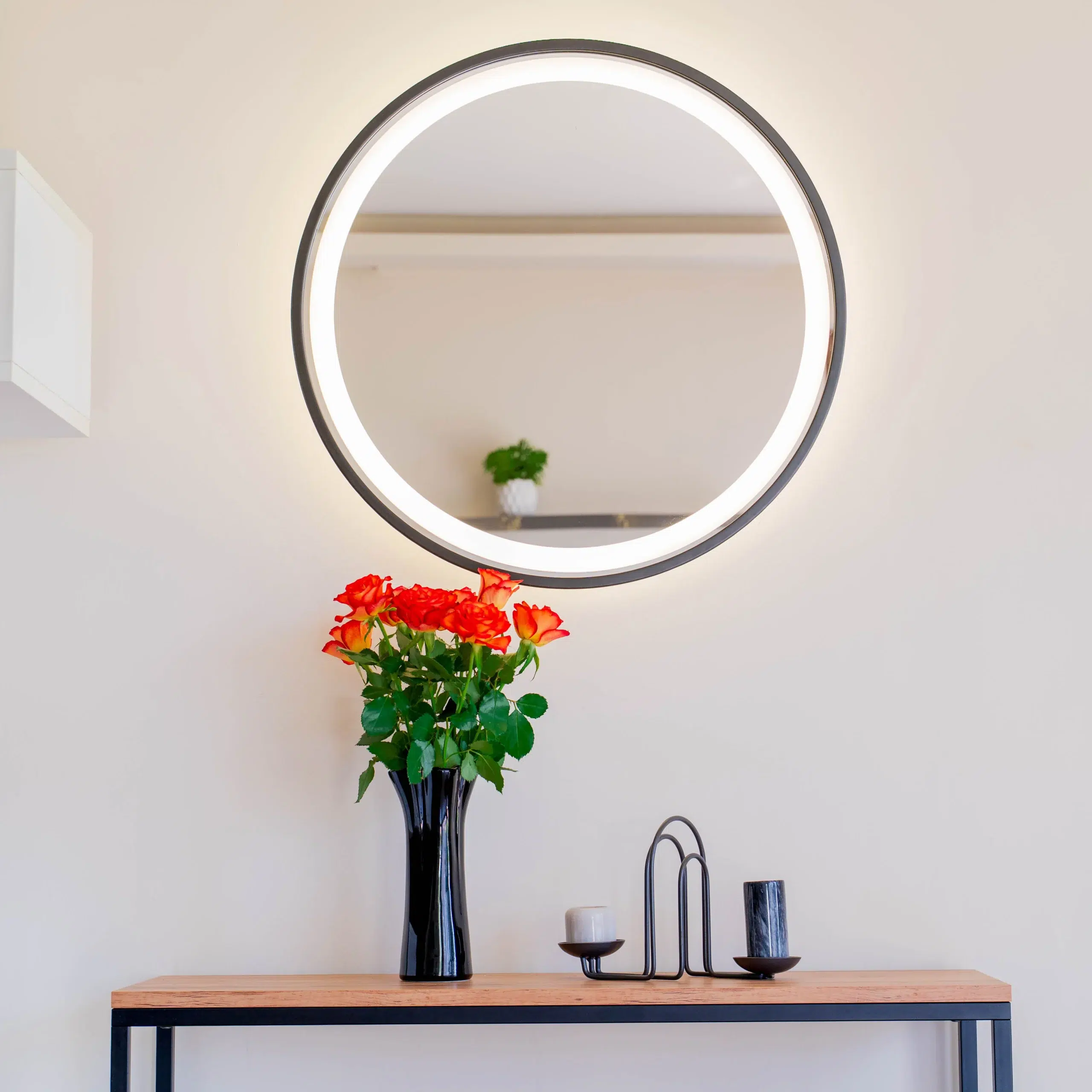 Okrągłe lustro łazienkowe LED w czarnej ramie, zawieszone nad umywalką w eleganckim nowoczesnym wnętrzu. Lustro LED w czarnej ramie jest dostępne w sklepie internetowym Magia Lustra – magialustra.pl.